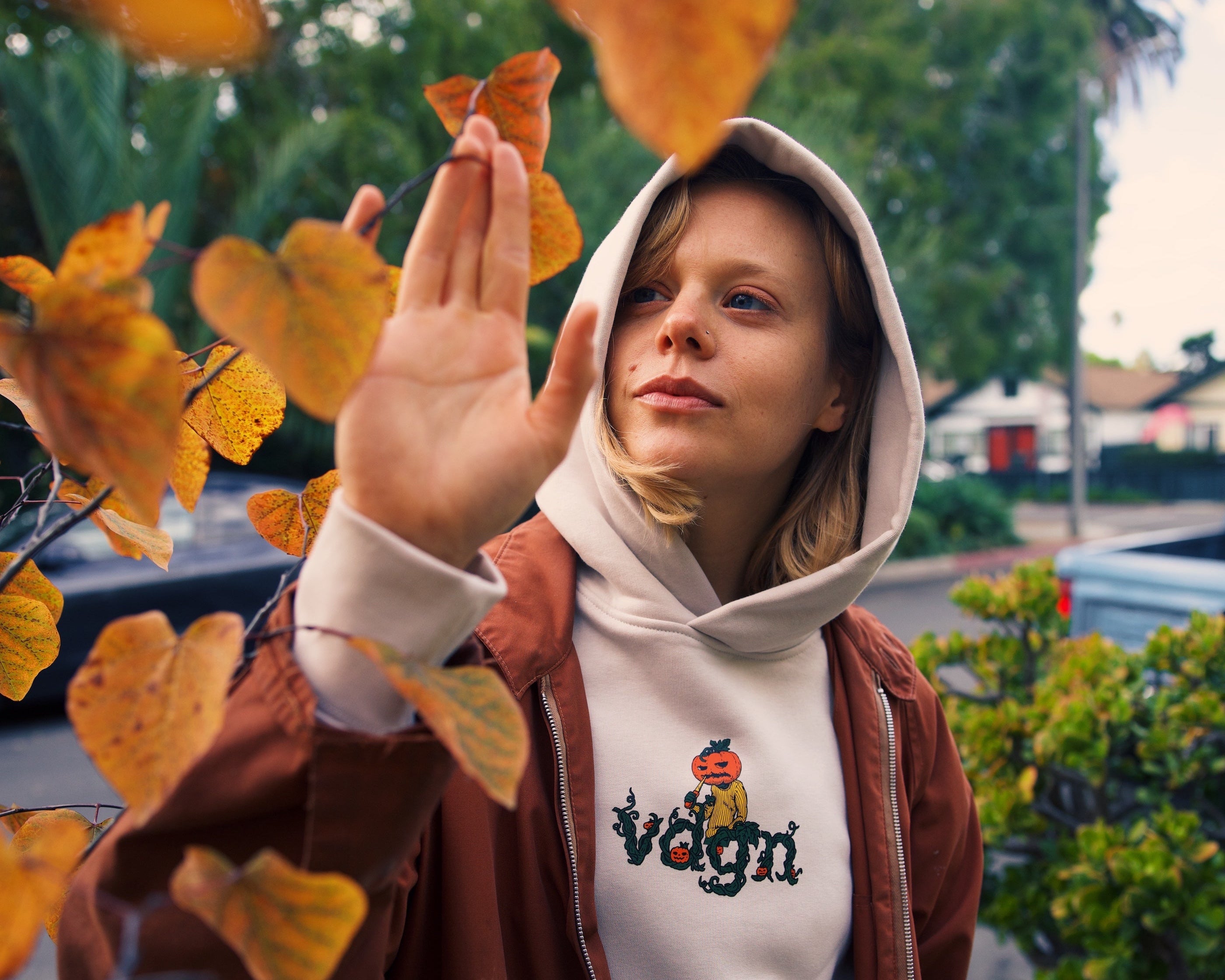 Person wearing a hoodie with a visible brand logo, standing outdoors with autumn leaves.